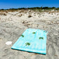 Coastal beach blanket with tassel edges and soft coastal print—your go-to for beach lounging and summer travel.